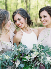 Ashley, the bride, smiling at her bridesmaid to her right while the bridesmaid to her left smiles and looks at them both.