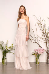 Woman in strapless gown with subtle ruffles posing by vases of flowers.