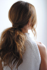 Image shows a brunette woman from the back so you can see her long hair tied back in a low ponytail.