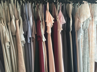 Image shows assorted flowy dresses in several colors all hanging on a rack. (Amsale)