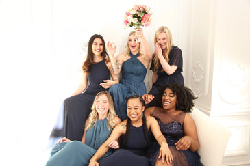 Three women smiling on a couch with three more women standing behind and smiling.