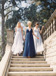 3 bridesmaids in different dresses (white, light blue, and navy) descending an outdoor staircase.