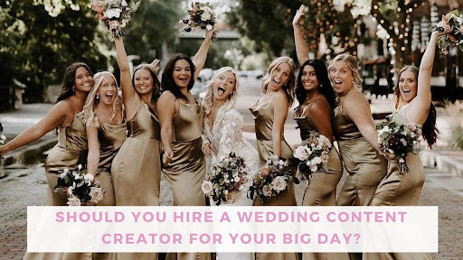 Bride in white in center of photo with four bridesmaids on each side of her in satiny dresses. Everyone is posing with arms up and mouths open in excitement and cheer.