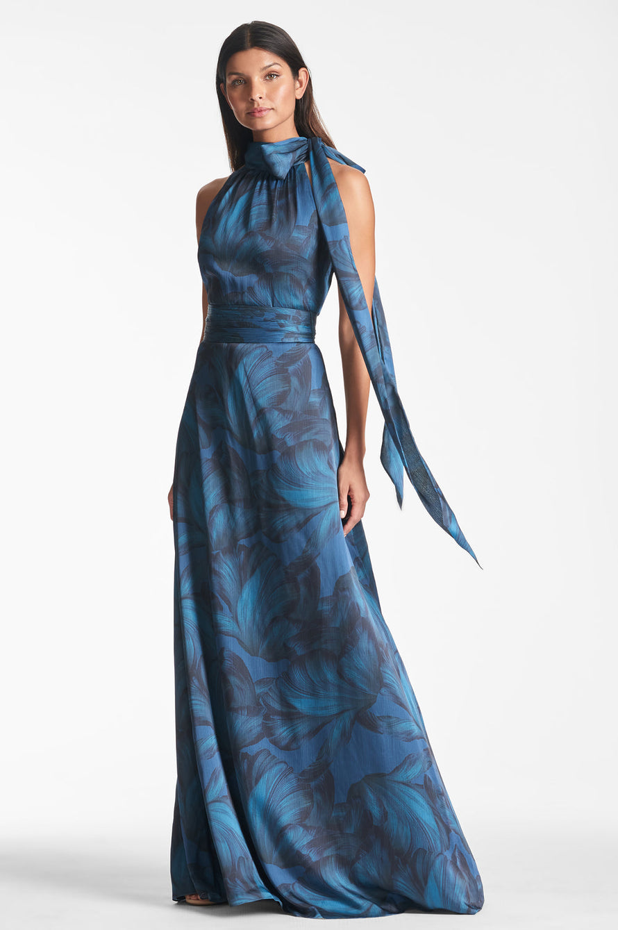 Model is wearing a floor length tonal petal dress with a fitted waist and halter neck.